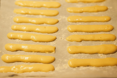 Raw dough for savoyardi cookies for making tiramisu cake lies on parchment paper