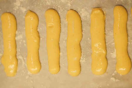 Raw dough for savoyardi cookies for making tiramisu cake lies on parchment paper