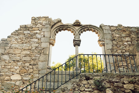 09 October 2023, Portugal, Evora - . view of old ancient stone ruins shows archway framed by intricate designs. green trees grow in background under clear sky. bright and highlights history of site.
