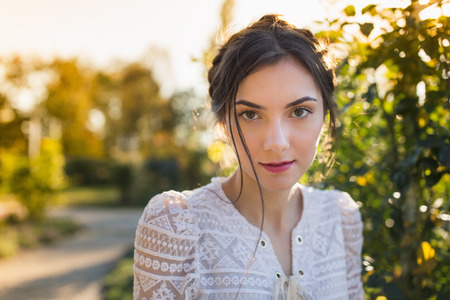 Beautiful brunette with braids around head in a stylish vintage white lace long sleeve blouse in an autumn parkの写真素材