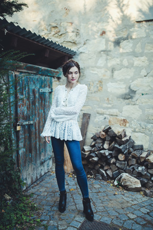 Beautiful brunette with braids around head in a stylish vintage white lace long sleeve blouse and jeans near the rural shedの写真素材