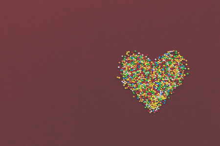 Heart made of rainbow sprinkles sugar decoration for cake on red background. Toned.の写真素材
