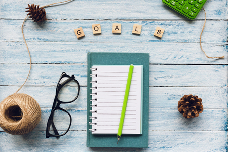 GOALS word and an empty notepad, book and glasses on a blue and white wooden background. Top view, flat lay. New Year resolutiontions to do list concept.の写真素材