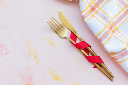 Golden cutlery in red ribbon and kitchen towel on a pink background . Spring holidays cooking and celebration concept. Top view, flat lay, copy space.の写真素材