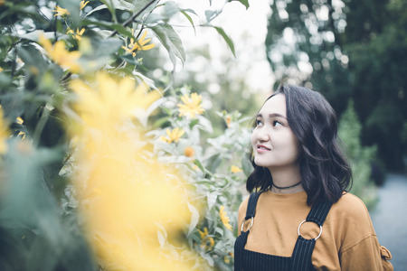 Beautiful asian girl in a garden, smiling, looking at yellow flowers, side viewの写真素材