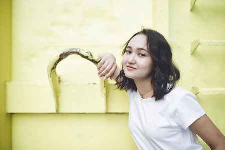 Optimistic asian girl in a white t-shirt, smiling, looking at the camera. Urban street portrait.