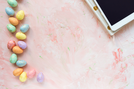 Pastel and gold colored eggs decoration, tablet computer and notebook on a pink background. Easter...