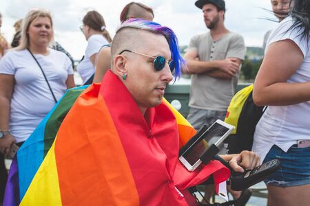 Prague, Czech Republic - August 11, 2018: People at the annual Prague Gay Pride parade. Hipster man in a rainbow flag in a wheelchair with a tablet in a crowd.のeditorial素材