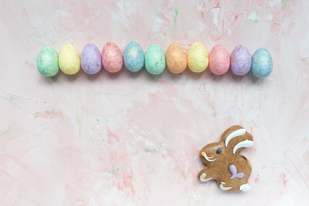 Pastel and gold colored eggs decoration and gingerbread easter bunny cookie on a pink background. Easter celebration concept. Top view, flat lay, copy space.の写真素材