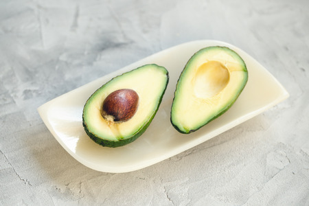 Two halves of fresh riped avocado on a plate on a gray background. Close up, selective focus.