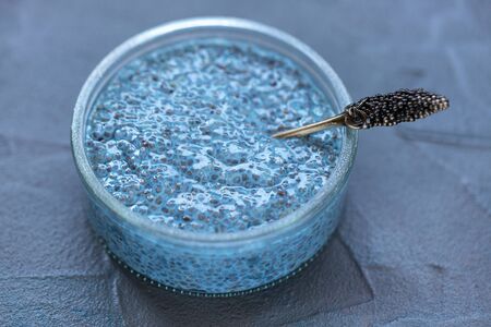 Blue spirulina or butterfly pea flower blue matcha powder chia seed pudding bowl and spoon. Close up, selective focus. Superfood and vegan trendy food concept. Moody dark gray background.の写真素材