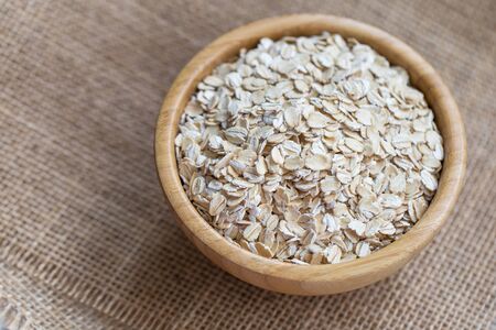 Oat flakes uncooked in a wooden bowl on a rustic piece of sackcloth, concept of healthy eating vegan...