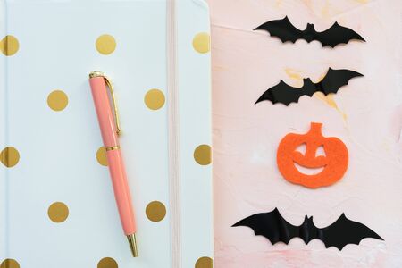 Notebook, pen, pumpkins and bats on a pink background. Halloween concept, flat lay, top view, social media hero header template, copy space.の写真素材