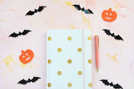 Notebook, pen, pumpkins and bats on a pink background. Halloween concept, flat lay, top view, social media hero header template, copy space.の写真素材
