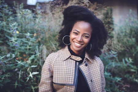 Beautiful african american young woman with afro and large hoop earrings in a stylish coat in a...