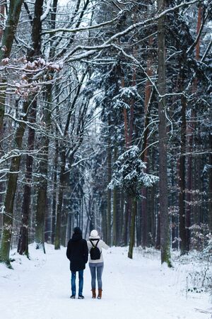 Unrecognizable young couple standing alone and looking towards a pathway in a winter forest. View...