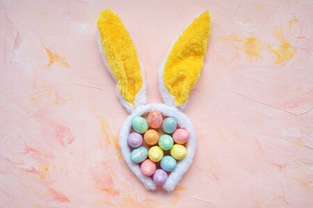 Pastel and gold colored eggs and bunny ears on a pink background. Easter celebration concept. Top...