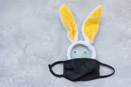 Easter during coronavirus concept. Bunny ears and mask on gray background. COVID-19 outbreak,...
