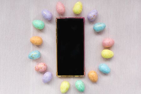 Pastel and gold colored eggs decoration and smartphone on pastel pink background. Easter celebration...