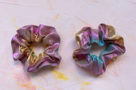 Two trendy holographic iridiscent shiny metallic scrunchies on pink background. Diy accessories and hairstyles concept, copy spaceの写真素材