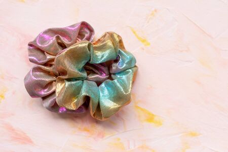 Two trendy holographic iridiscent shiny metallic scrunchies on pink background. Diy accessories and hairstyles concept, copy spaceの写真素材