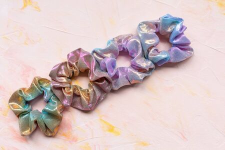 Four trendy holographic iridiscent shiny metallic scrunchies on pink background. Diy accessories and...
