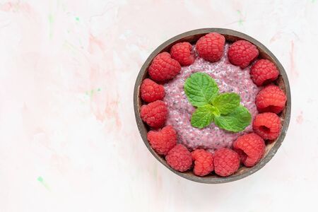 Chia seed pudding with almond milk, yogurt and pitaya dragon fruit powder, raspberries and peppermint leaves in coconut bowl. Superfood and vegan food concept. Pink background, copy spaceの写真素材