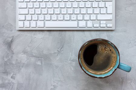 Cup of black coffee and computer keyboard on gray rustic backround. Flat lay, top view, copy space, social media template, morning and internet conceptの写真素材