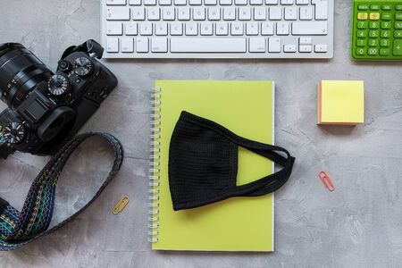Freelance photographer quarantine home office background. Mask, camera, keyboard, notepad and calculator on gray. Coronavirus quarantine lockdown over concept. Top view, flat lay, copy spaceの写真素材