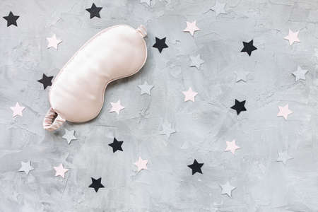 Pink satin eye sleepink mask and pink and sillver paper stars confetti on gray background. Sweet dreams concept. Close up copy space, flat lay. Accessories for girls and womenの写真素材