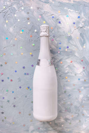 White champagne party bottle and colorul metallic stars confetti on blue background. Flat lay, copy space. New year and Christmas celebration concept.の写真素材