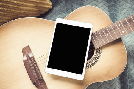 Acoustic guitar and digital tablet on a couch at cozy home background. Online music lessons, learning playing or writing songs and hobby concept. Top view, flat lay, mock upの写真素材