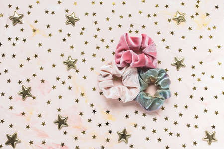 Three trendy velvet pink and holographic shiny metallic scrunchies and golden stars confetti on pink...