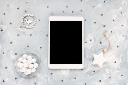Digital tablet, chocolate and stars decoration on desk workspace, blue background. Winter shopping,...