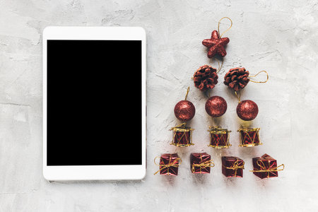 Digital tablet and red Christmas decoration on desk workspace, gray background. Winter shopping, celebration, To Do List, distance learning, lifestyle concept. Top view, mock up, copy spaceの写真素材