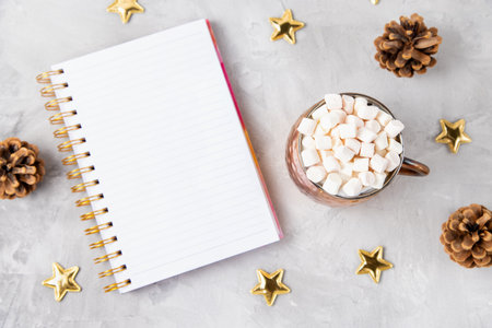 Copper mug with cocoa or chocolate and marshmallows on top, gold stars and pine cones Christmas decoration on light gray background. Winter hot beverage concept, copy spaceの写真素材