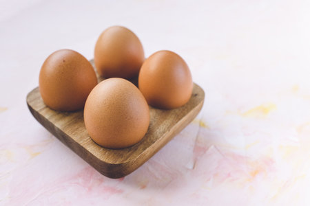 Four brown eggs in a wooden storage organizer box on pink background. Useful household items, organic healthy bio product and Easter holiday concept. Close up, copy spaceの写真素材