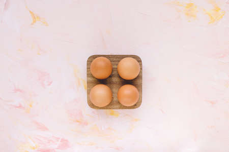 Four brown eggs in a wooden storage organizer box on pink background. Useful household items, organic healthy bio product and Easter holiday concept. Top view, copy spaceの写真素材
