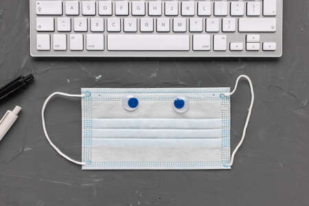Man home office. Mask, computer keyboard, pens on gray background. Working from home on internet or...