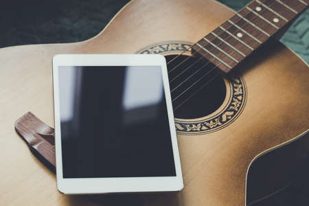 Acoustic guitar and digital tablet on a couch at cozy home background. Online music lessons, learning playing or writing songs and hobby concept. Top view, flat layの写真素材