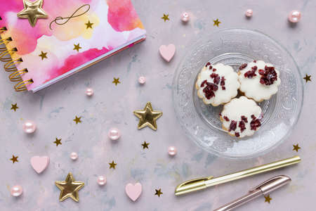 Notepad, pens, cookies on pink background with stars, hearts and pearls. Woman home office,...