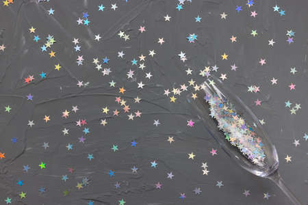 Champagne flute glass on black with colorful stars confetti festive background. Christmas holiday,...