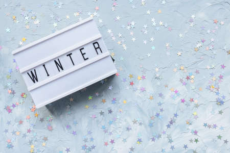 Text WINTER on white and blue with stars confetti festive background. Winter season and holidays concept. Flat lay, copy spaceの写真素材