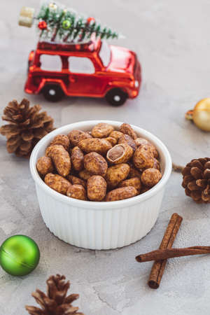 Candied or sugared almonds with honey and cinnamon in small porcelain bowl on gray with Christmas decoration background. Traditional Christmas sweets for holidays. Copy spaceの写真素材