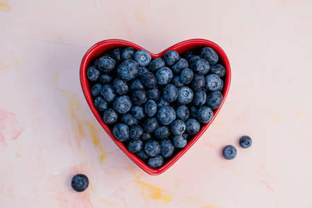 Blueberries in heart shaped red bowl on pink background, concept of healthy eating vegan food and snack. Close up, selective focus, copy spaceの写真素材