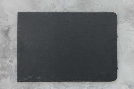 Slate plate on gray stone texture background. Kitchen stone tray for serving food. Black granite rectangle board. Empty space for menu or recipe. Top view copy space, mockupの写真素材