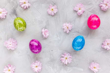Colorful eggs and spring pink sakura cherry blossom flowers on gray background. Easter celebration...