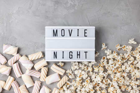 Text MOVIE NIGHT with popcorn and marshmallow on gray background. Cinema, movies, entertainment and snacks movie snacks at home concept. Top view, copy spaceの写真素材