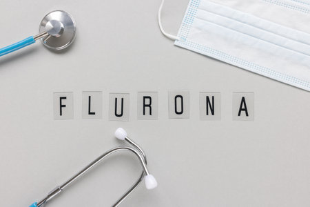 Word FLURONA on gray with face mask and stethoscope background. COVID and flu double infection. First combination of two viruses, respiratory coinfections conceptの写真素材