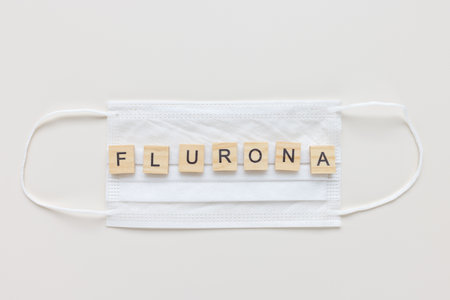 Word FLURONA on medical mask, white background. COVID and flu double infection. First combination of two viruses, respiratory coinfections concept. Top view, copy spaceの写真素材